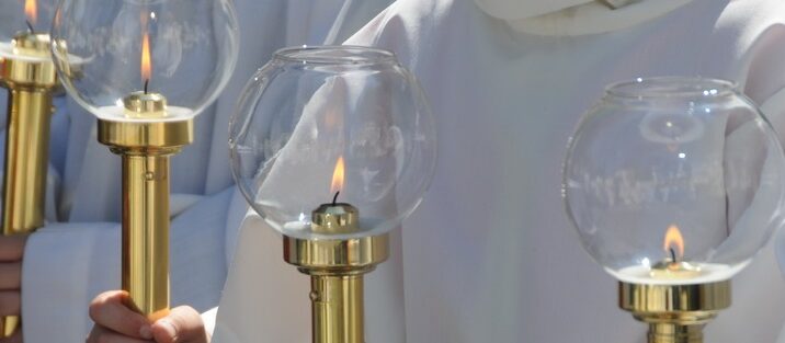 Mehrere Messdiener halten goldene Flameaus in der Hand.